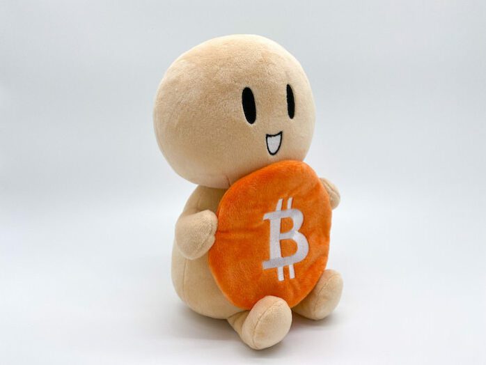 Bitcoin Plüschtier The Little Hodler sitzt auf dem Boden und hält eine Bitcoin Münze in beiden Händen